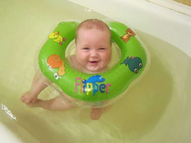 Новорождённый купается в ванной с кругом на шее