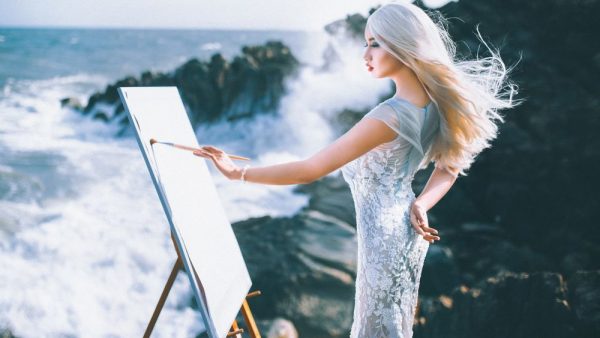 Девушка на побережье рисует на мольберте