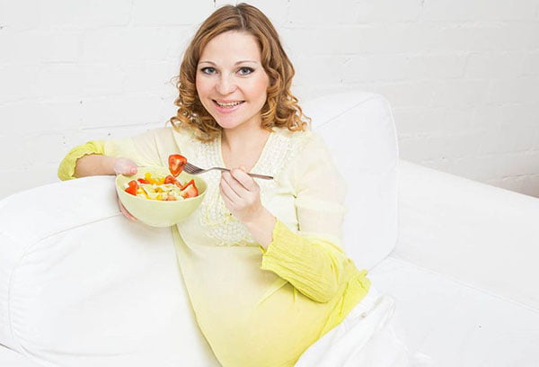Беременная женщина ест кашу с фруктами